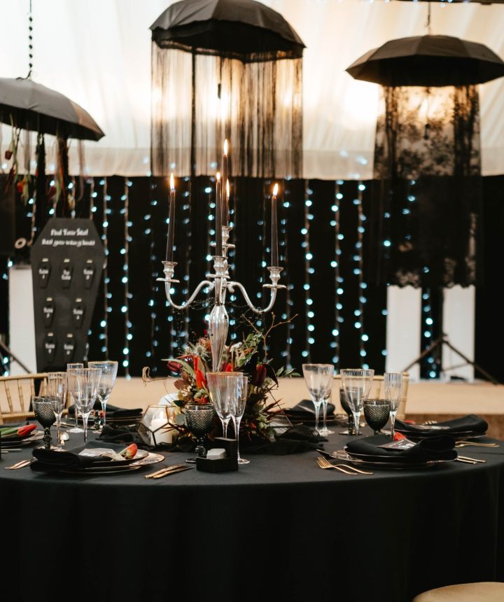 A marquee styled in black and gold with hanging black parasols and a silver candelabra