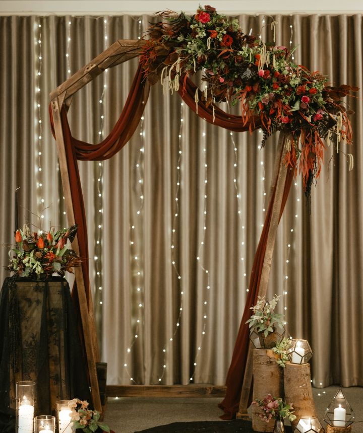 An autumn ceremony arch with rust-coloured drape, dried stems and candlelight