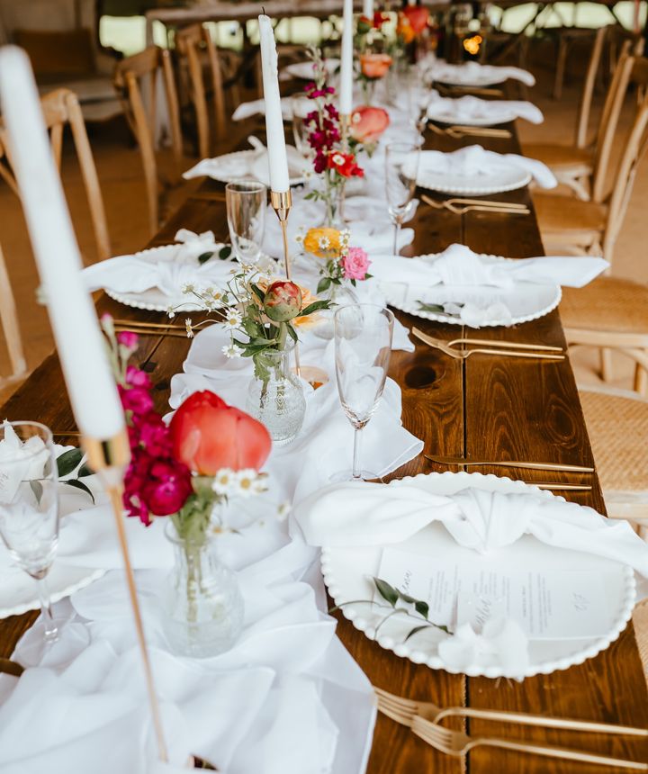 Long trestle tables laid with white runners, bud vases of coral flowers and gold cutlery